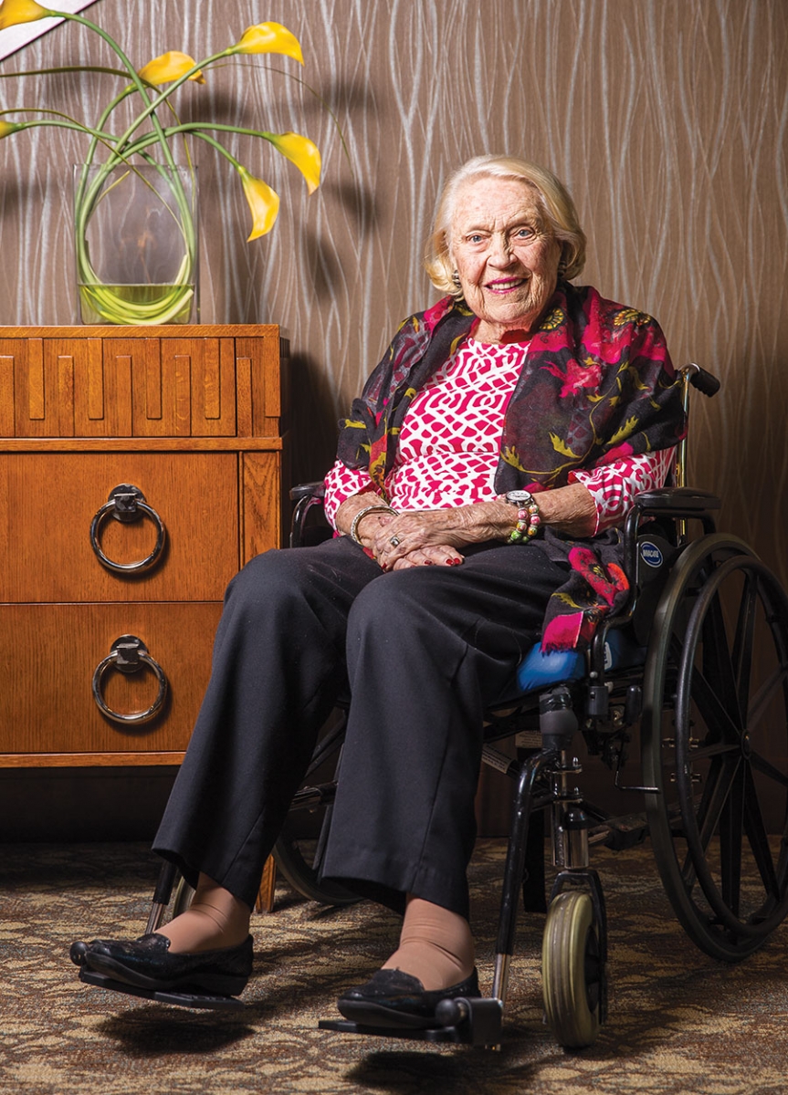 A portrait of Sally Pillsbury sitting next to a dresser with a vase of yellow flowers perched on top.