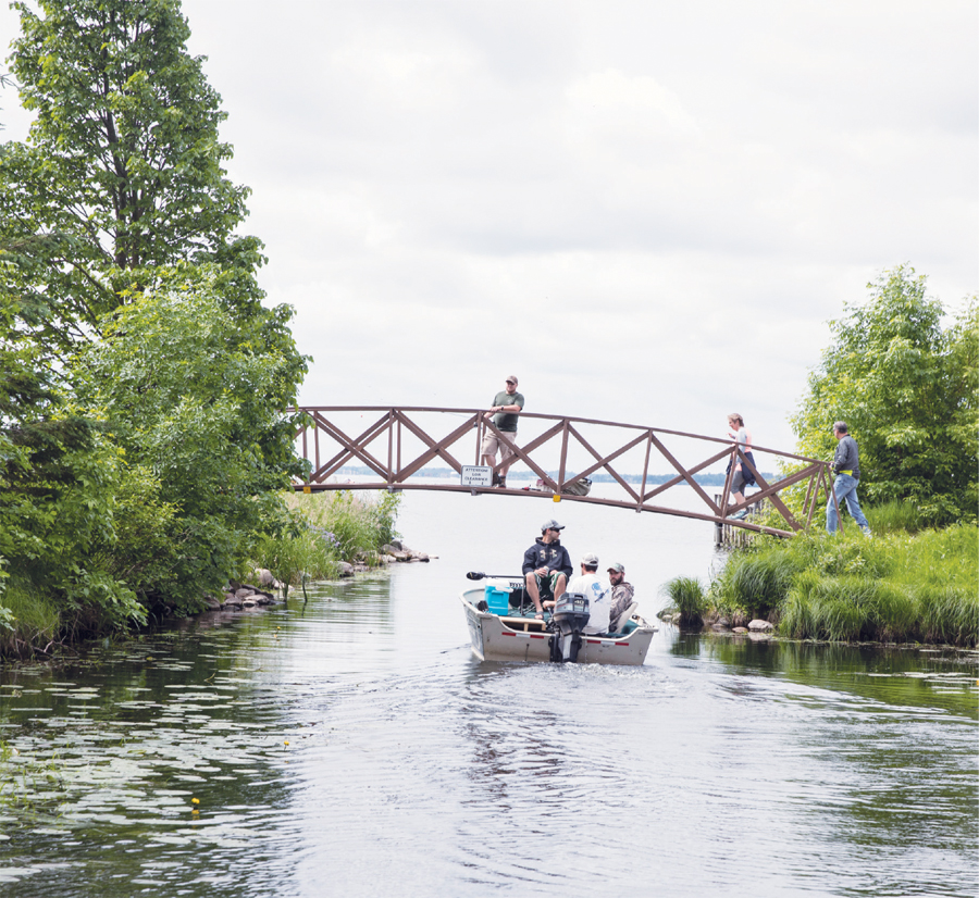 A boat rides under a bridge with people standing on it.